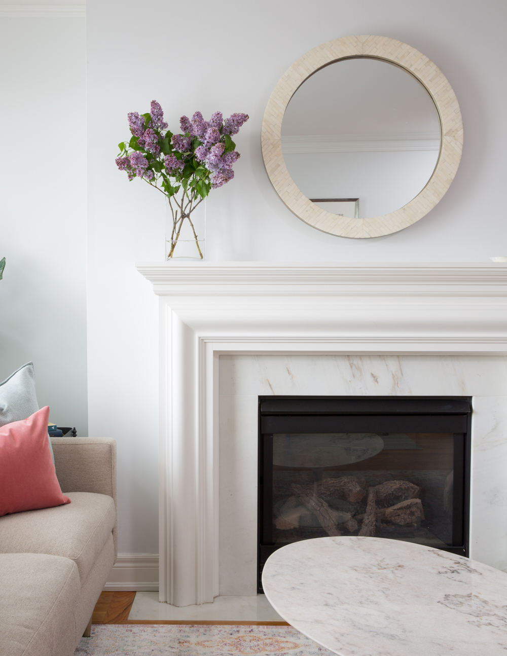 round mirror and lilacs over fireplace