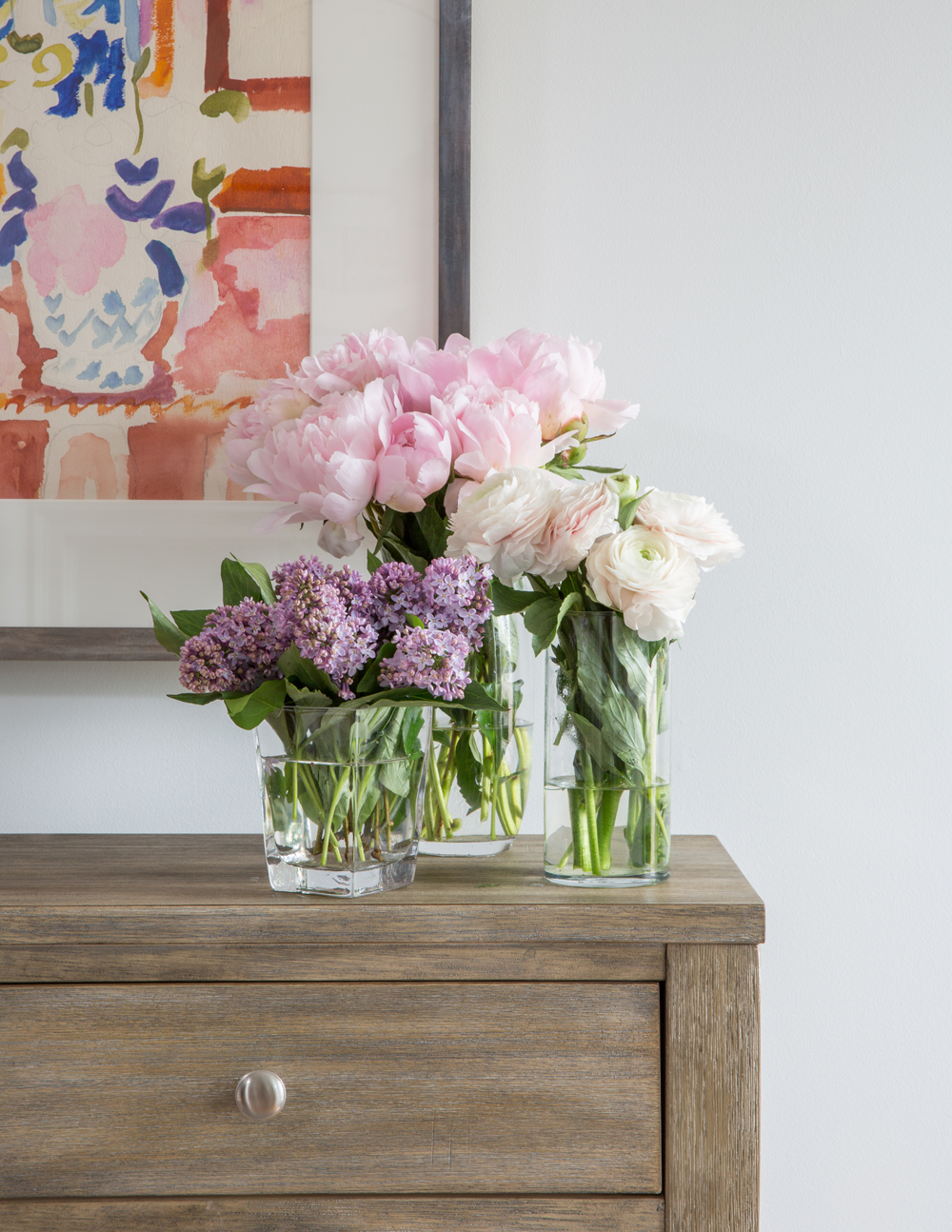 fresh peonies, lilacs and roses on wood table top with drawer and round knob