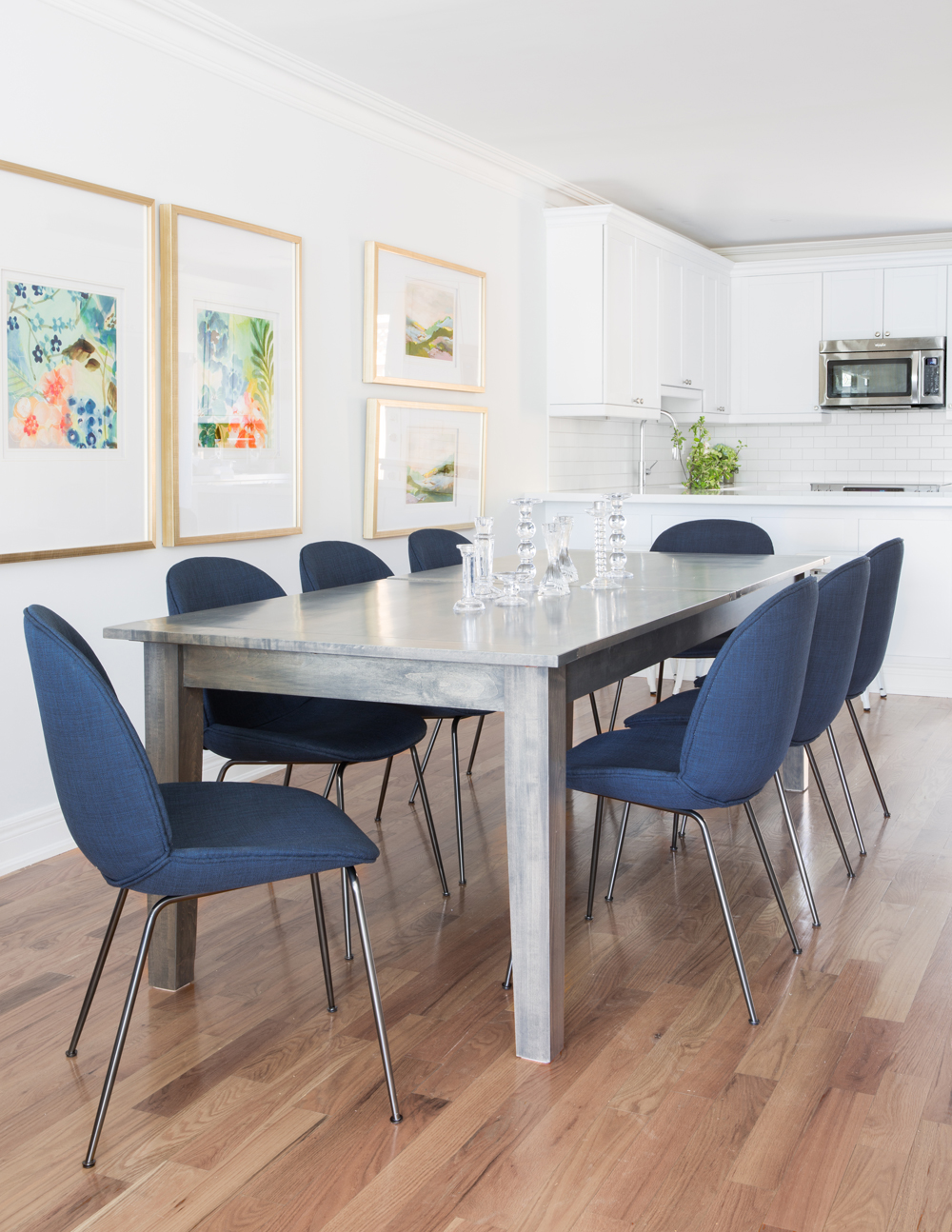 dining room table with eight blue fabric chairs with chrome legs, white kitchen in background