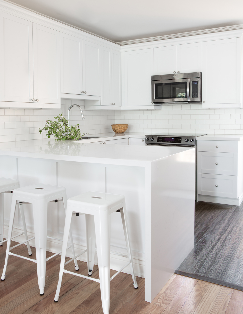 white kitchen with grey floor, white island with three white metal stools, greens in sink