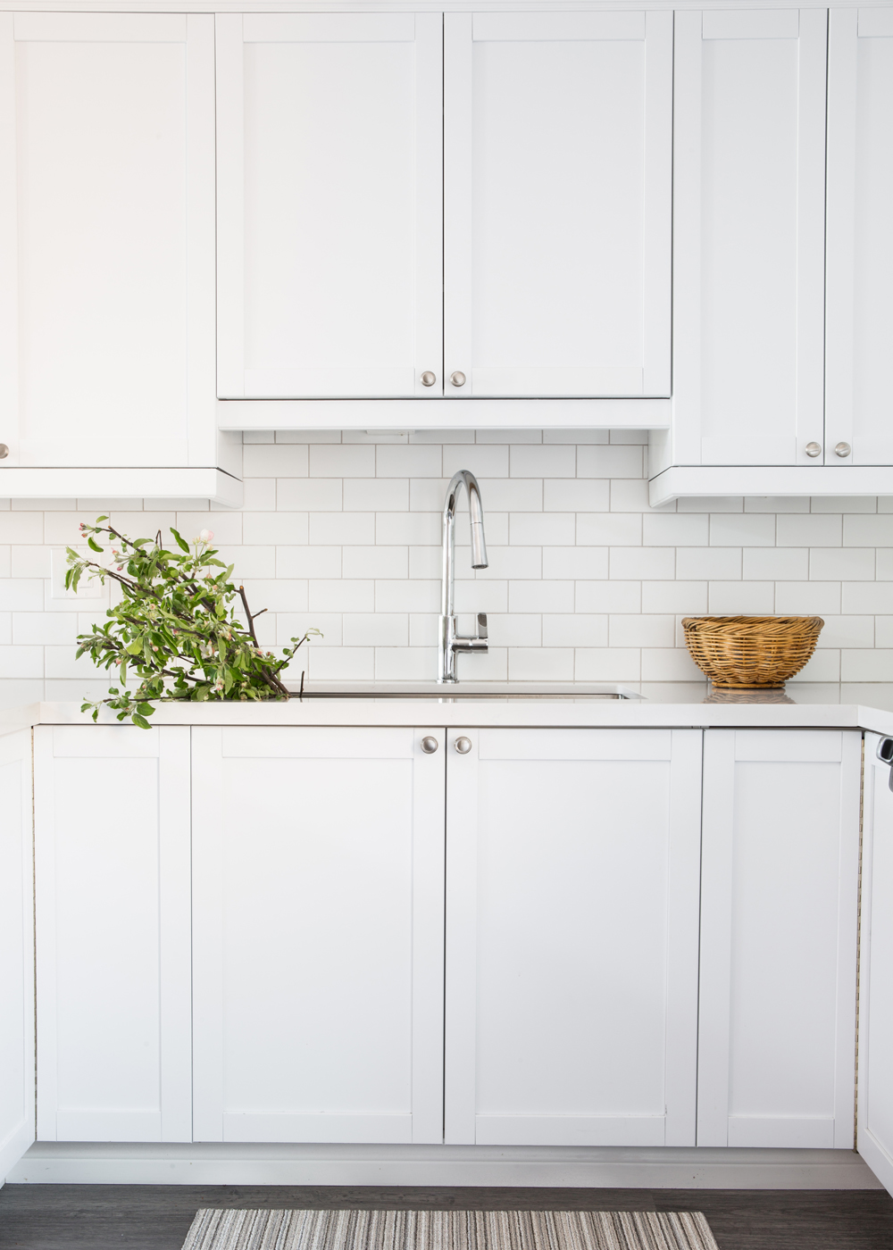 white kitchen cabinetry with round metal knobs, single sink faucets, greens in sink, wicker basket on counter