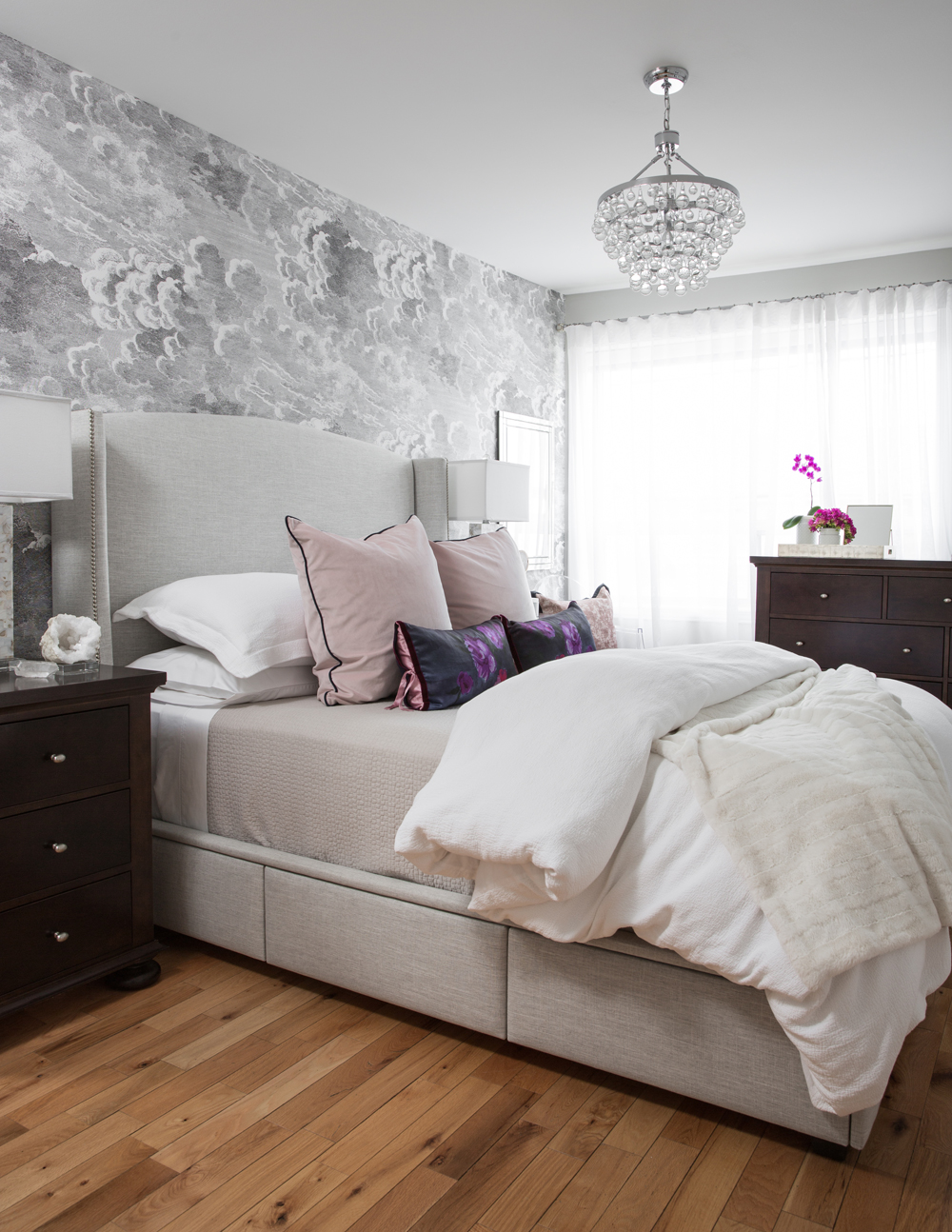 bedroom with grey cloud wall paper, chandelier, wood floors and dark dressers