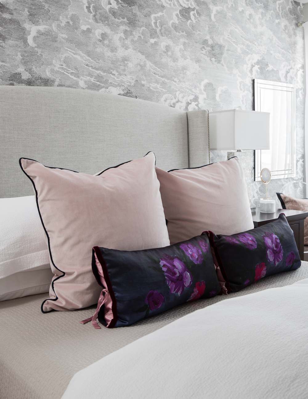 closeu up of bed with two large pink cushions with black trim and two dark floral smaller cushions in front