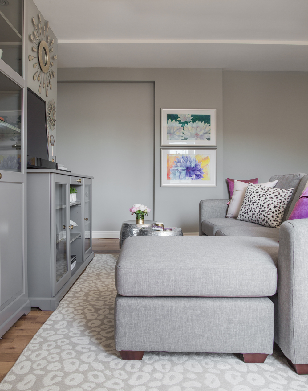 end of grey sectional facing grey cabinets, TV, two framed floral drawings