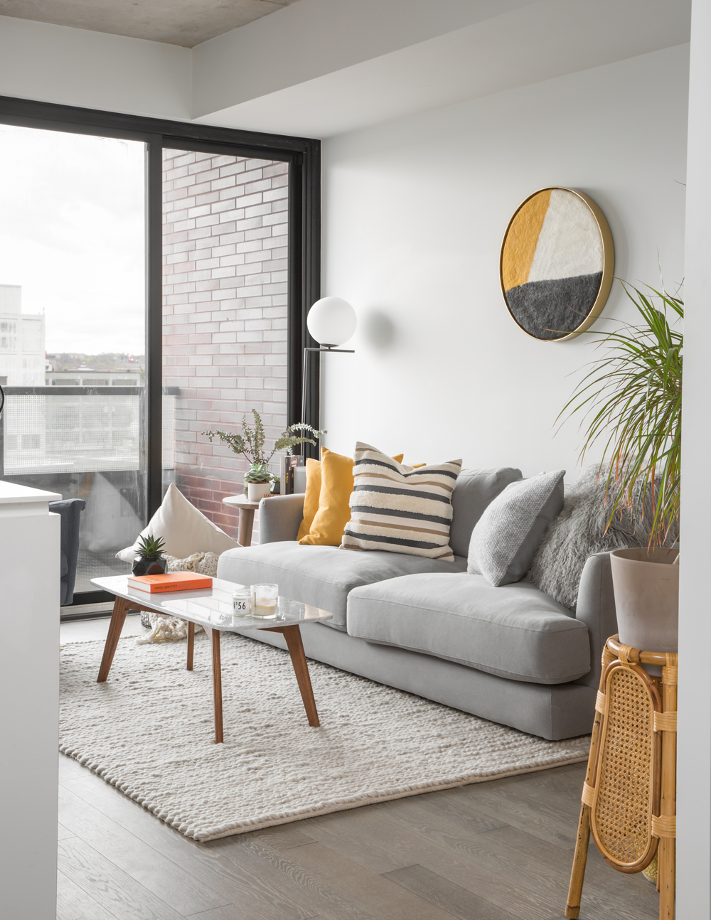 grey sofa, round wall hanging, black framed windows to balcony in condo living area