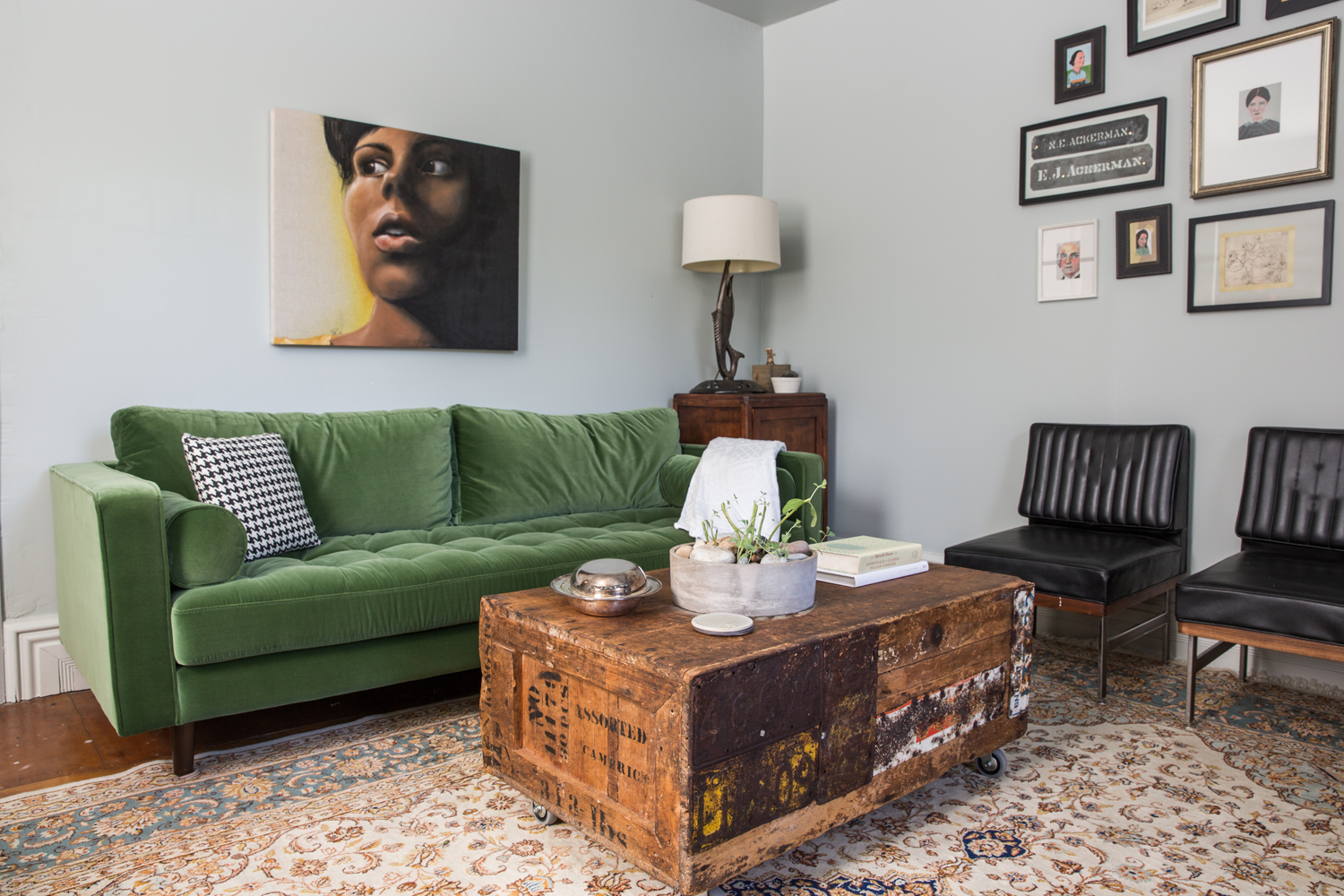 Eclectic farmhouse living room with a beat-up coffee table and rich tufted green sofa.
