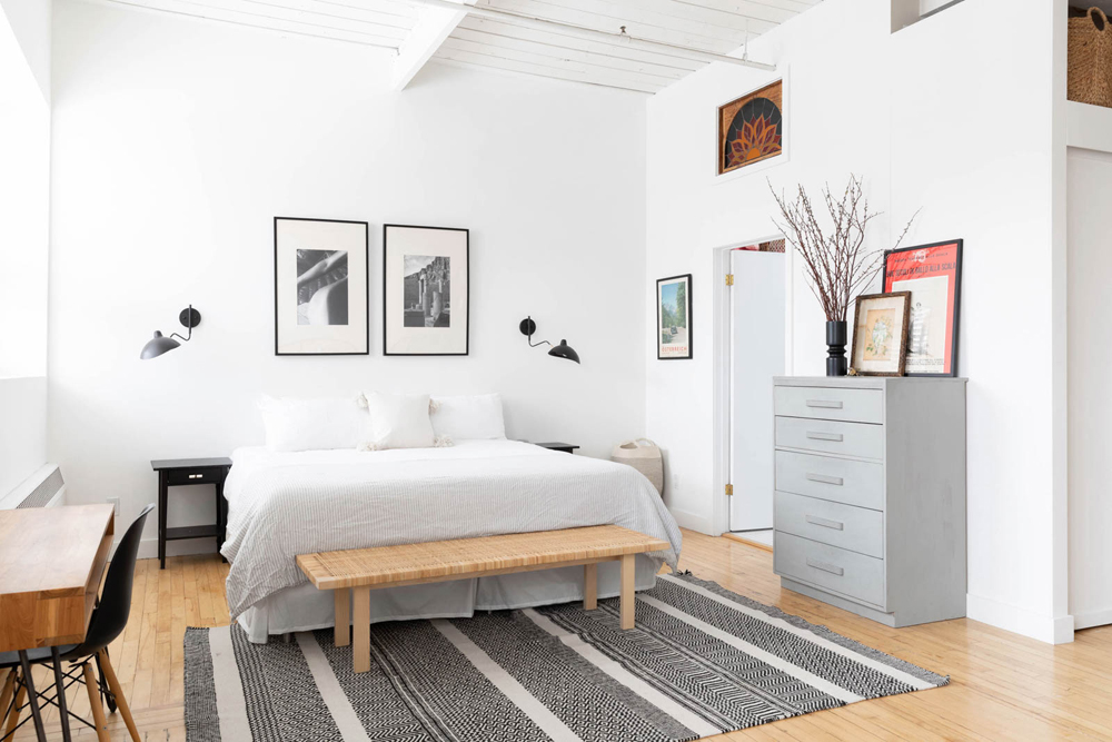 All-white bedroom with two matte-black wall sconces and vintage art