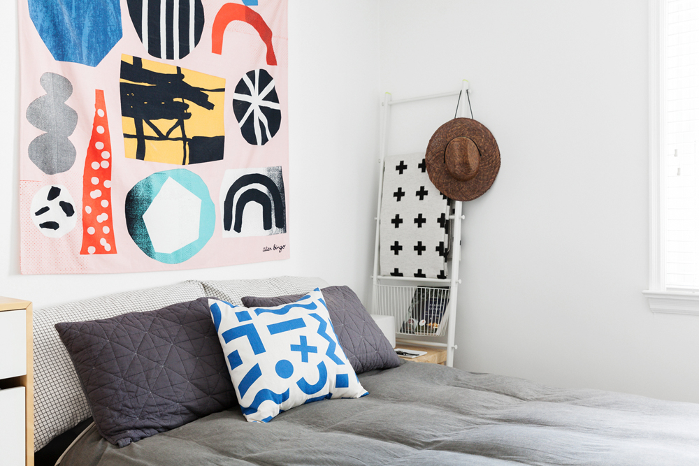 All-white bedroom with pop of colour from patterned tapestry and throw pillows