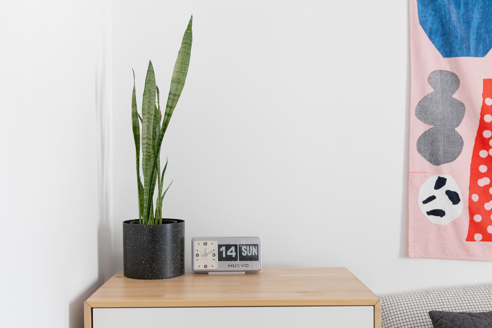 A bedside table that doubles as a dresser with an alarm clock and potted plant on top