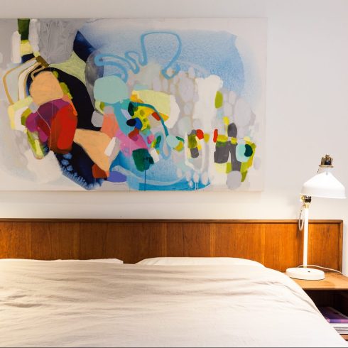 A brightly coloured piece of artwork hanging over a bed