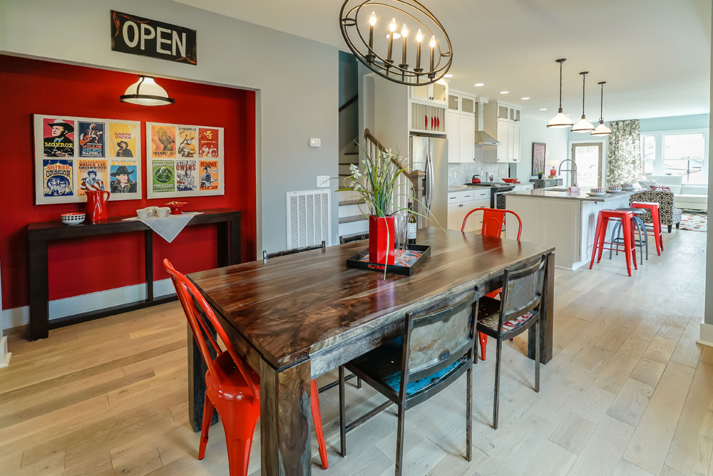 An open-concept dining room and kitchen space with vintage decor, hardwood flooring and red furniture and accent wall