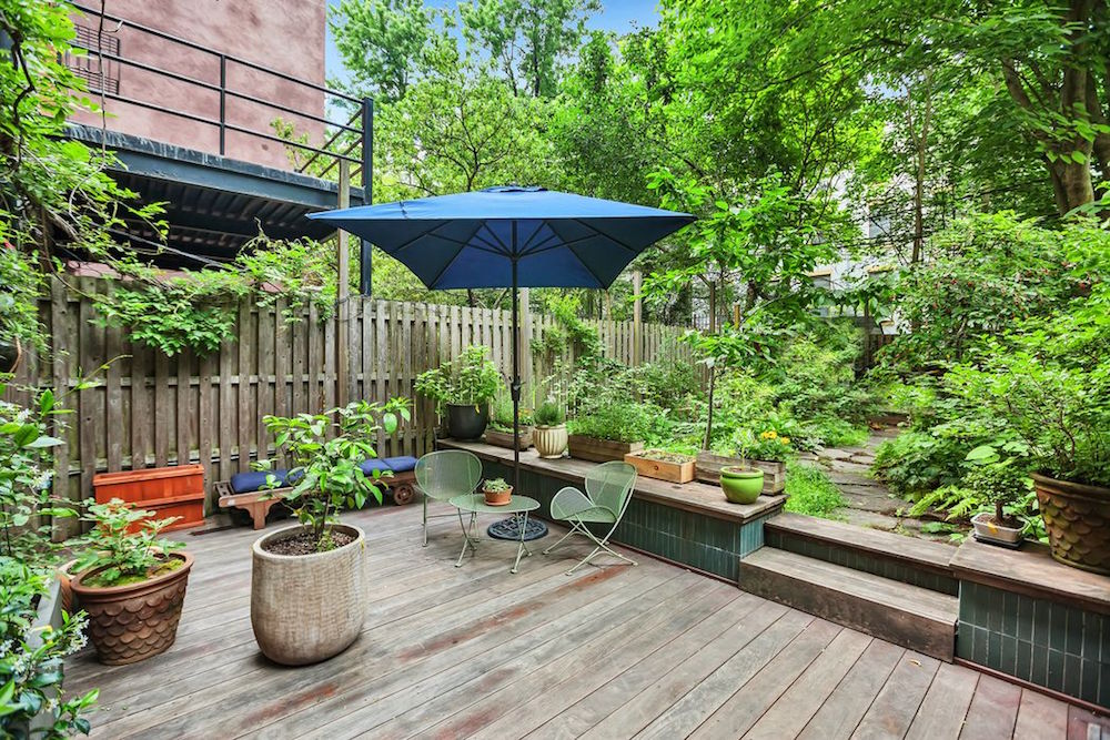 wooden back patio with wooden fence, blue umbrella and green plants
