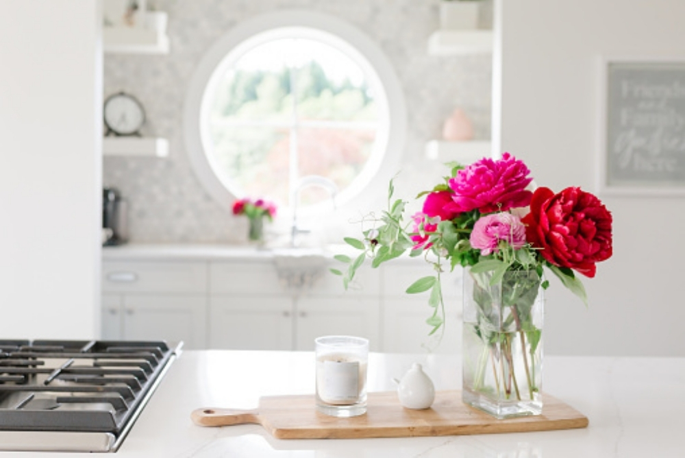 A pink bouquet of flowers and a candle in a bright white kitchen
