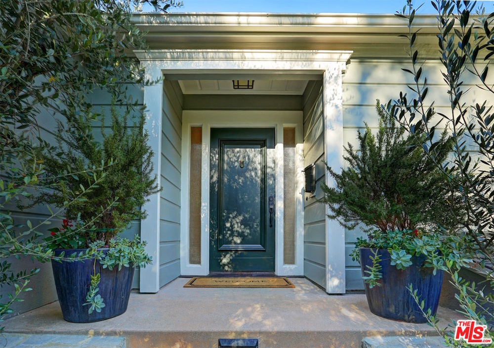 green front door on blue house with welcome mat and blue-potted bushes at front