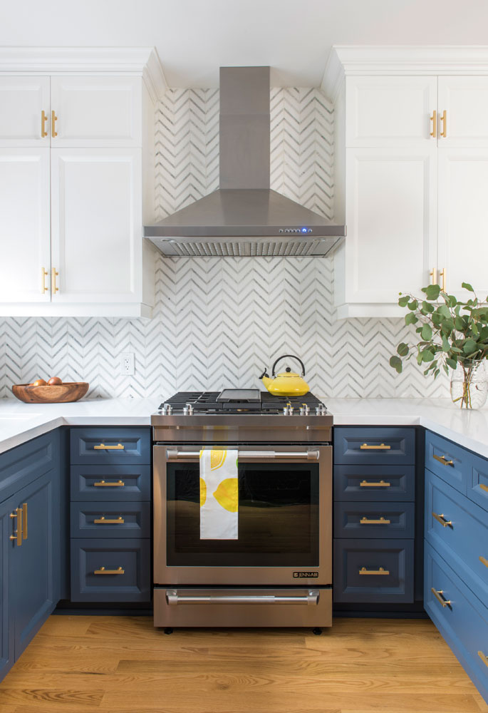 Kitchen with two-tone blue and white cabinetry, brass hardware and herringbone backsplash.