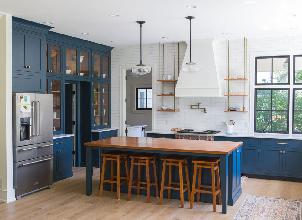 Spacious kitchen with dark blue lower cabinets, white backsplash, wood elements and open shelving.