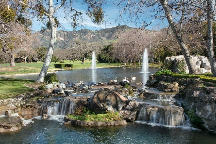 A large pond, featuring swans and waterfalls, with a stunning view of the mountains in the distance