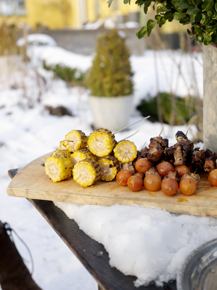 Grilled corn, meat and tomatoes on BBQ in snow-covered backyard