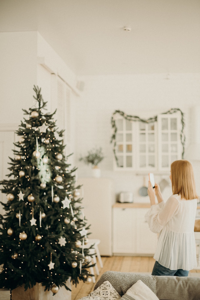 woman taking photo of green christmas tree with gold decorations and white lights