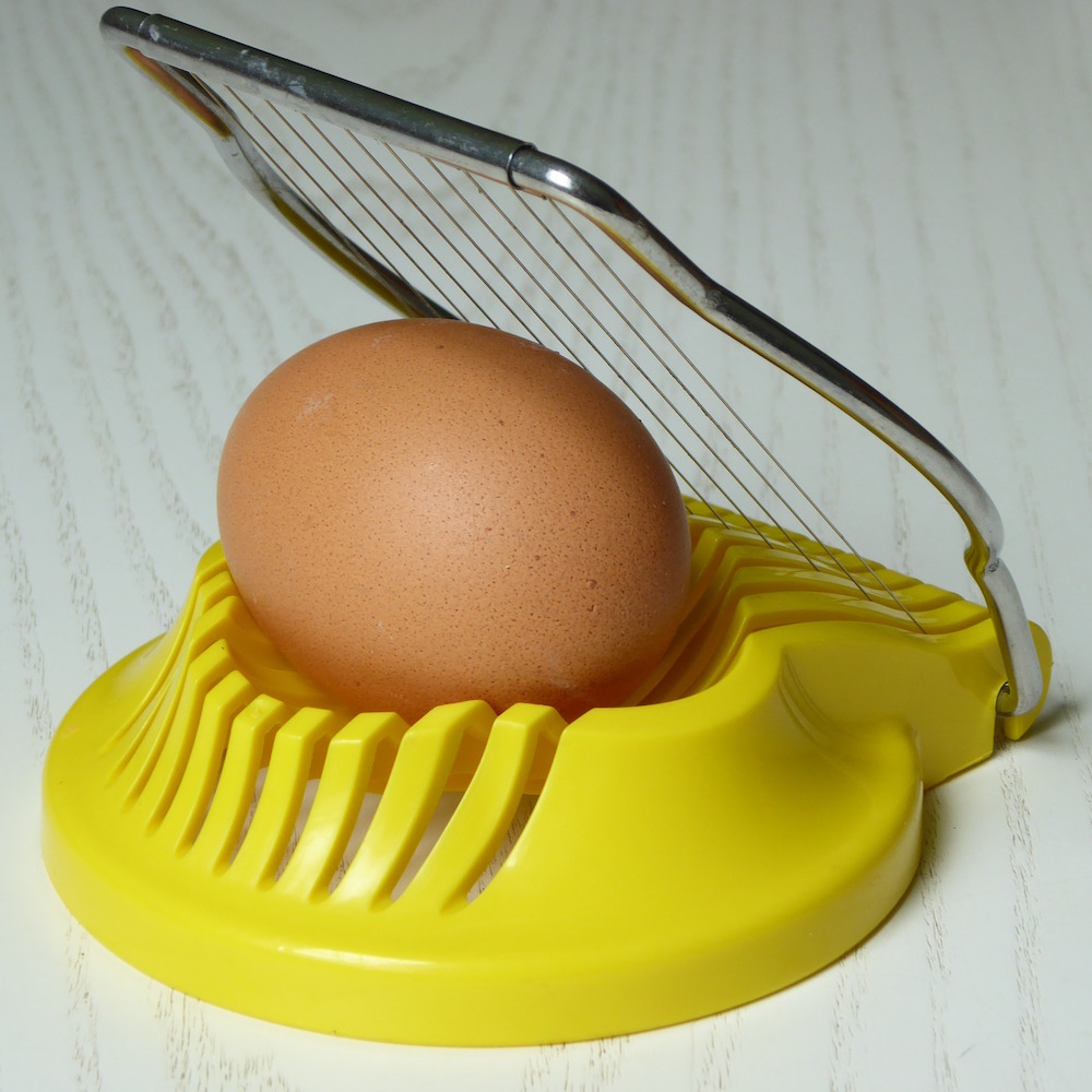 yellow egg slicer machine with brown egg on white surface