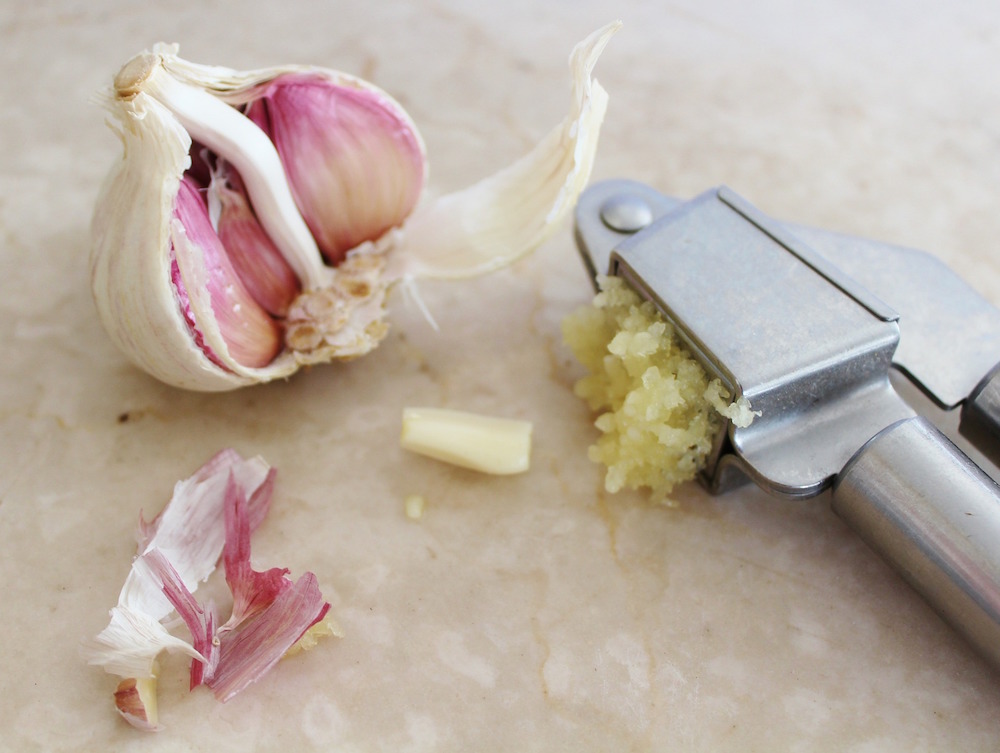 metal garlic press and garlic on beige surgace