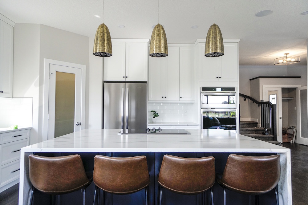 three metallic pendant lights in all-white kitchen with centre island