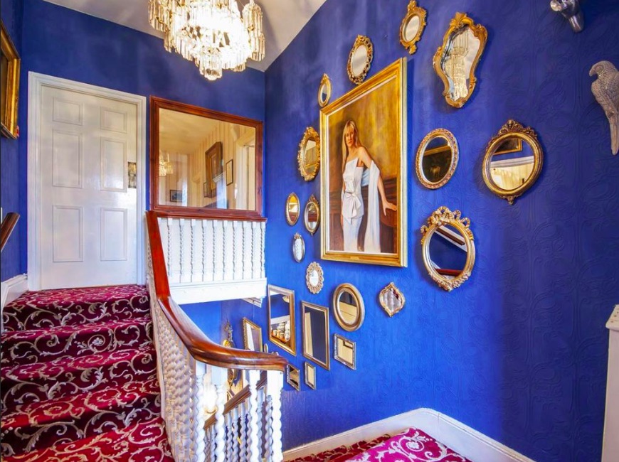 Bright, spacious staircase with family portraits, blue paint and burgundy carpeting