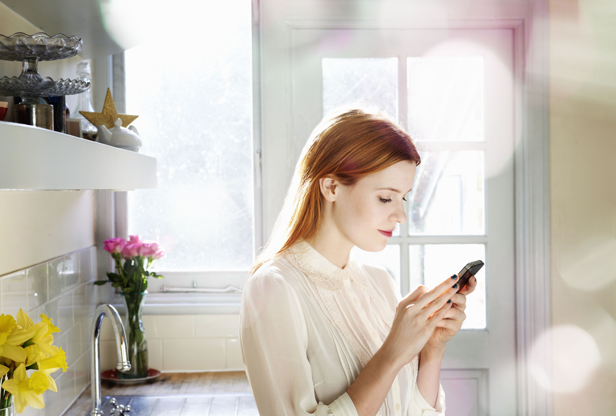 Woman texting on phone in kitchen