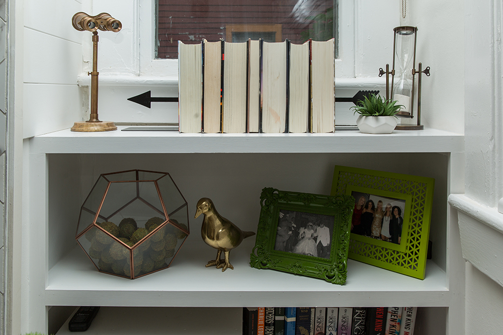 Bookshelf styled with green frames and gold accents