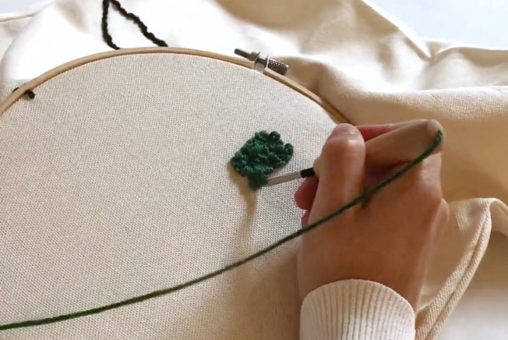 Person embroidering a punch needle pillow case