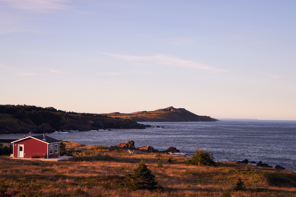 scenic view of the ocean with a small red house on the rolling landscape
