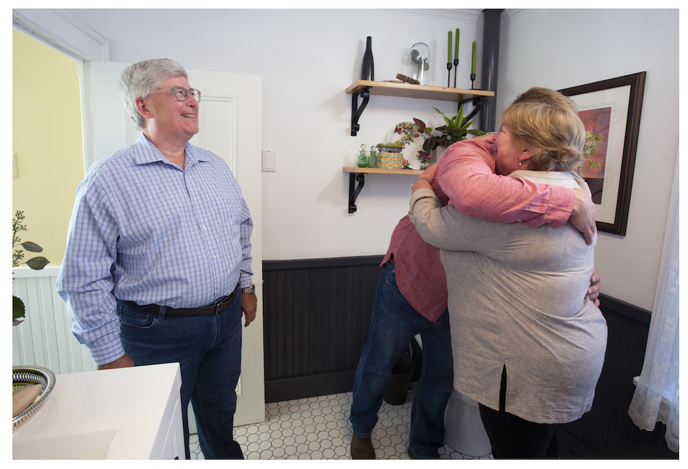 Randy hugs Martha while Glenn smiles in the renovated bathroom