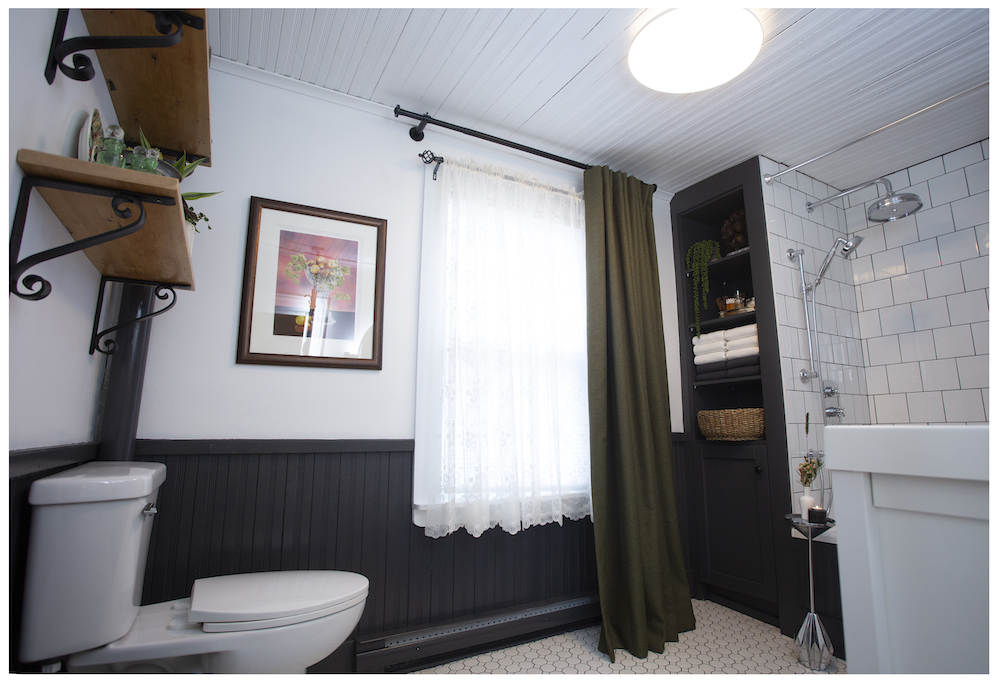 the renovated bathroom with dark lower panels and green curtains
