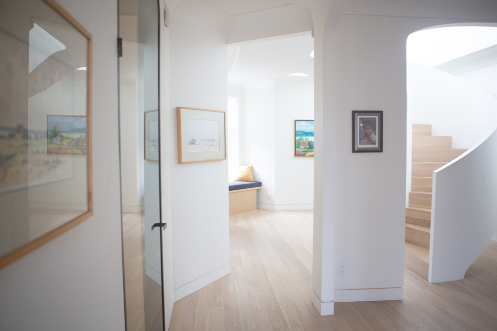 modern hallway with glass door on left, artwork, curved stairs on right