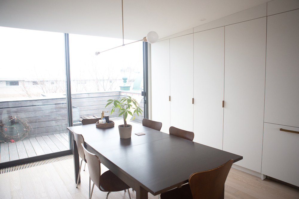 dining table, six chairs, wall of sliding glass doors, two bulb chandelier, right wall of white cabinetry