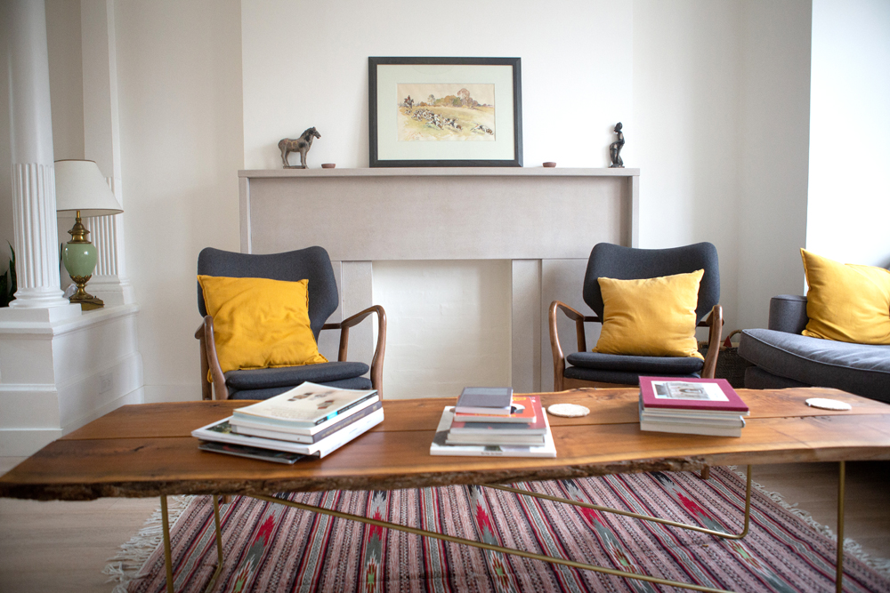 two grey chairs with yellow cushions, frame of fireplace, wood table with books