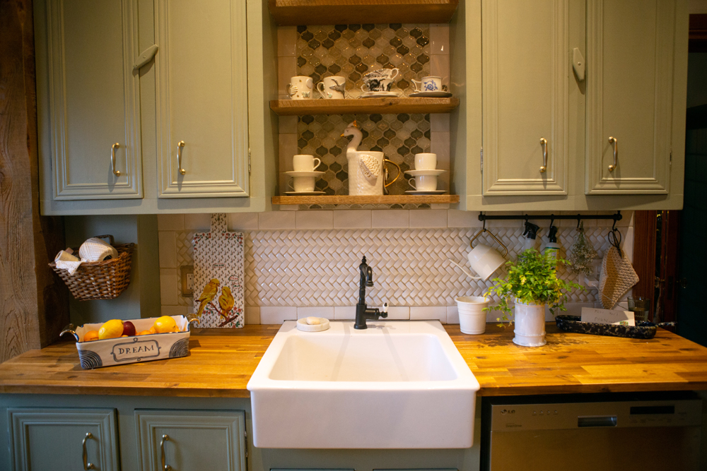white kitchen sink surrounded with sage-green cabinets and tile backsplash