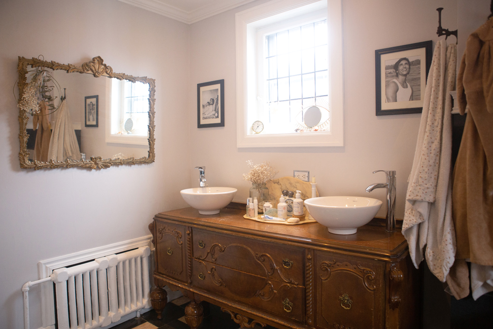 bright bathroom with vintage mirror, ornate cabinet and double white vessel sinks