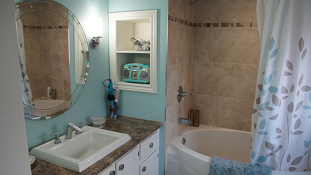 An outdated bathroom with older tub and single sink vanity.