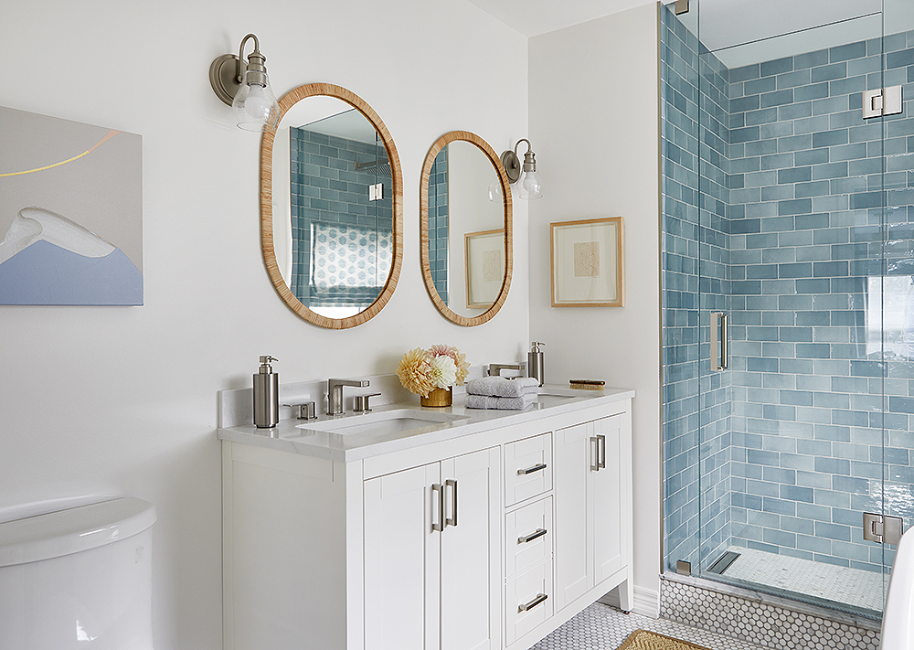 A bathroom with a double vanity and shower with blue tiles