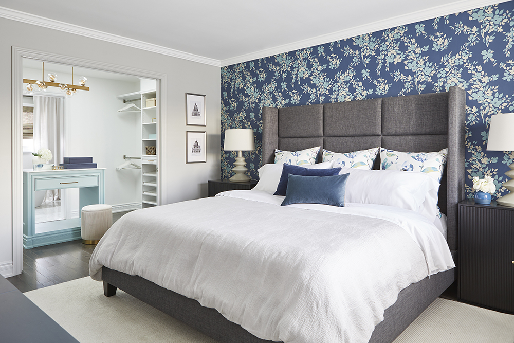 A large king-size bed in a bedroom with a feature wall covered in floral prints.