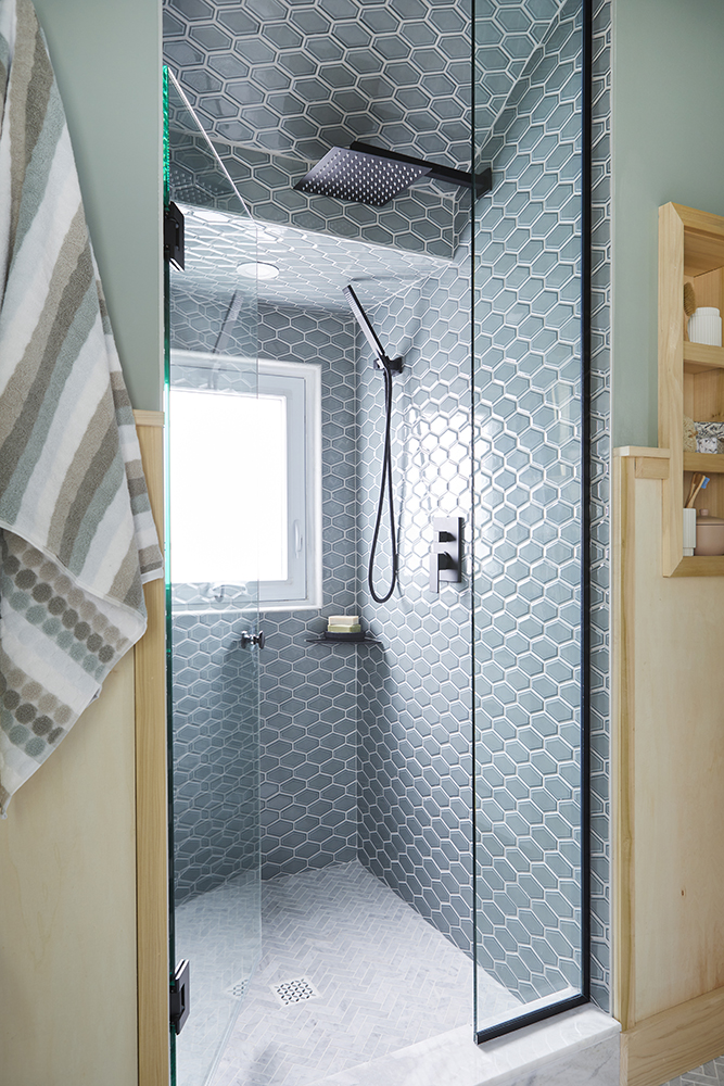 A tall shower stall with blue tiles and herringbone floor.