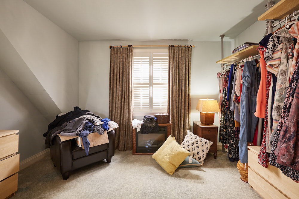 grey bedroom with clothes hanging from racks and clothes on chair