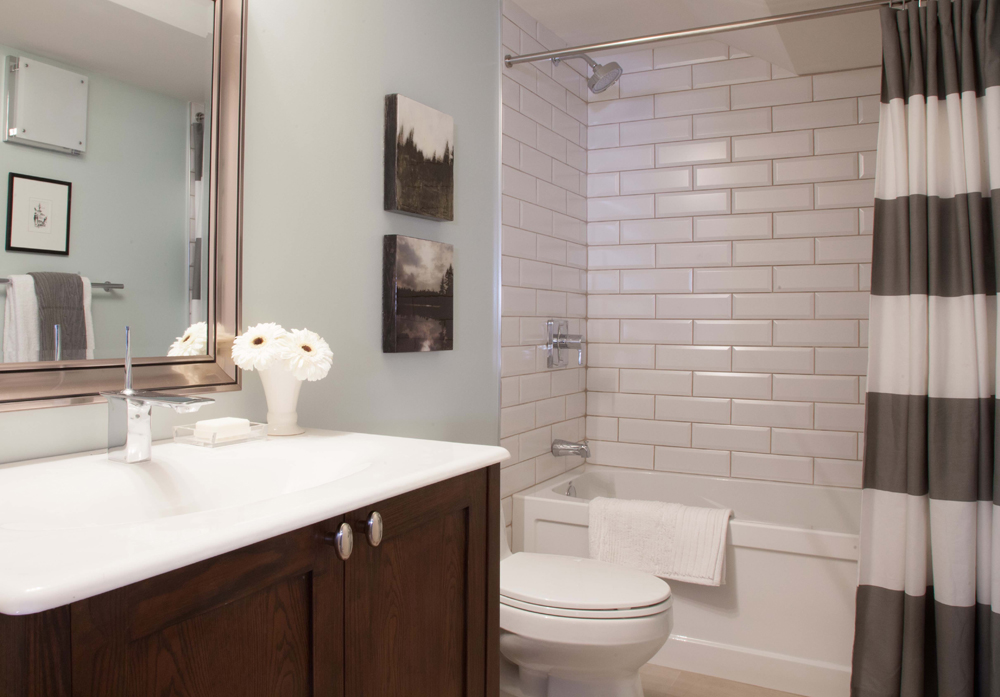 A washroom with subway tile as a backsplash in the shower, with a cute vanity sink and mirror.
