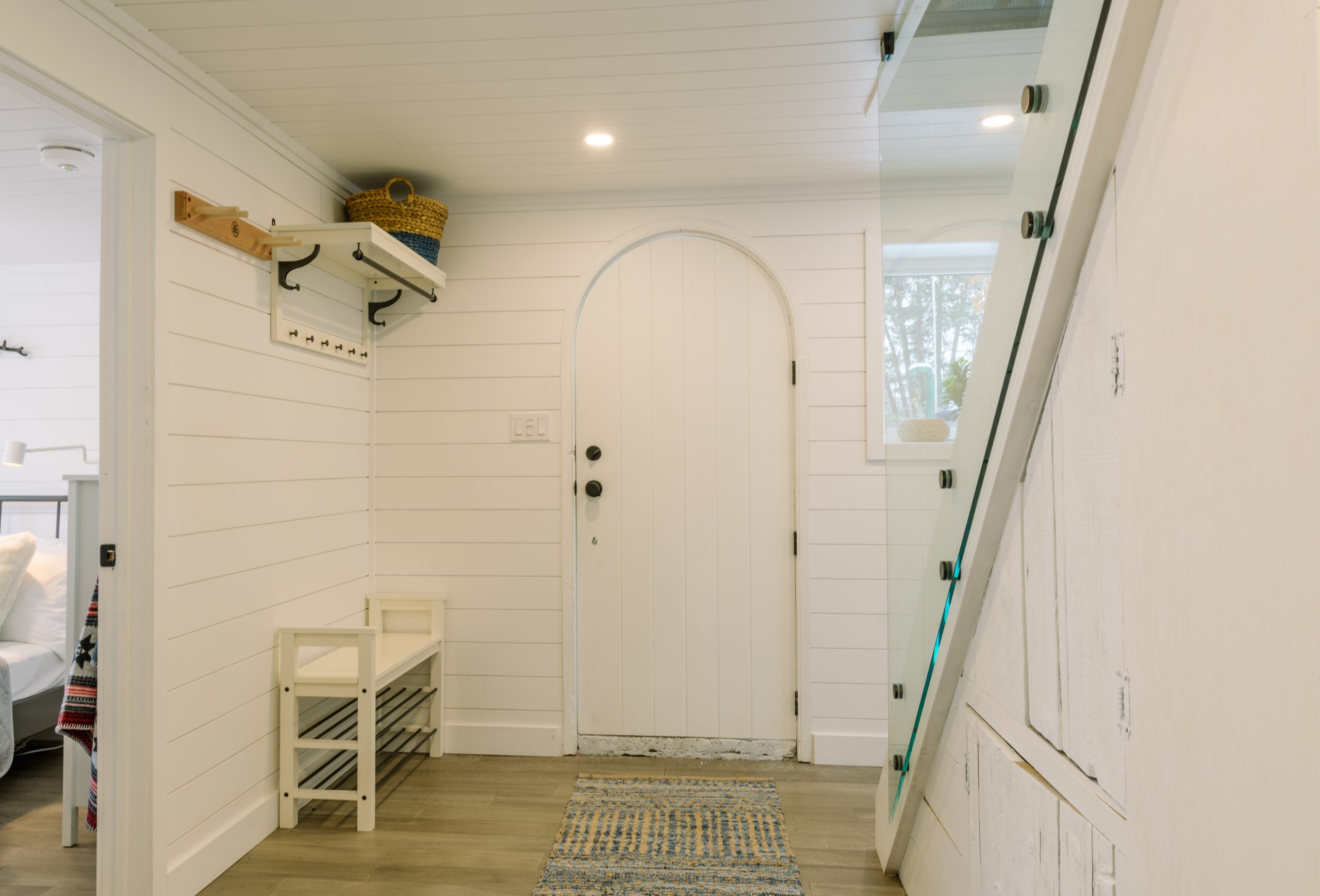 bright white foyer with coat hooks and glass staircase