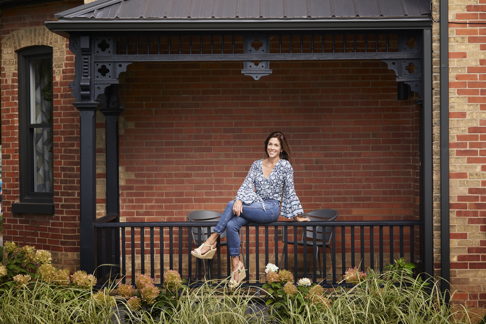 Sarah Richardson sitting on the porch railing of a home she recently renovated