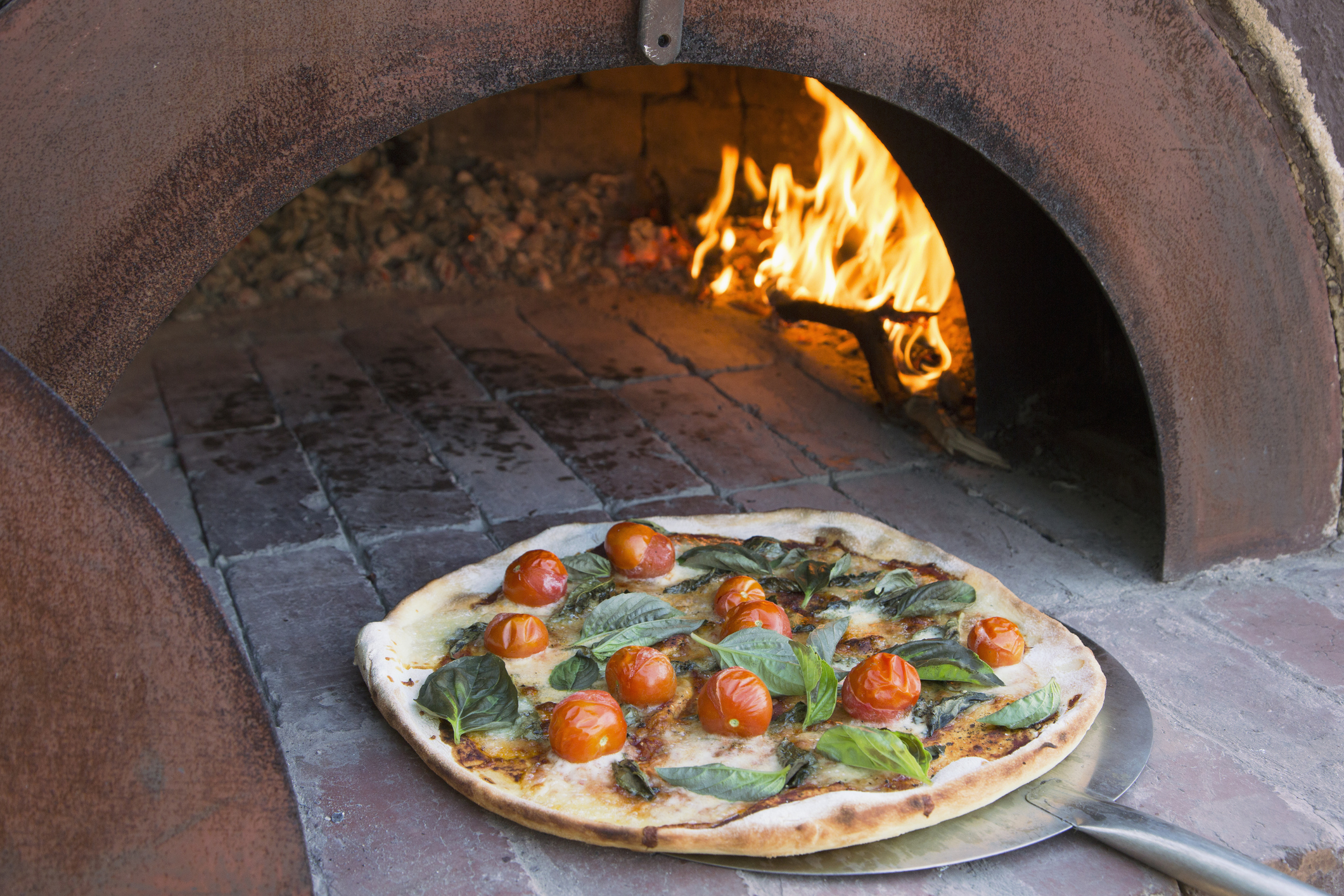 Pizza coming out of an outdoor pizza oven