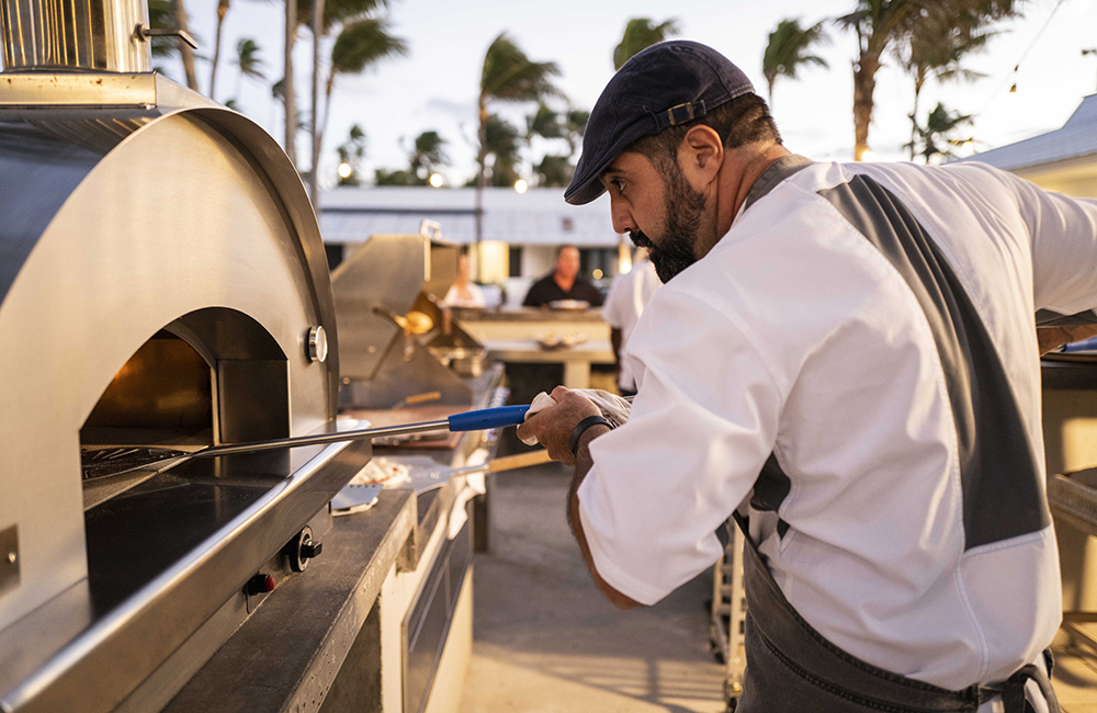 Sebastian putting a pizza into the pizza oven at the dining bar at the Island of Bryan resort.
