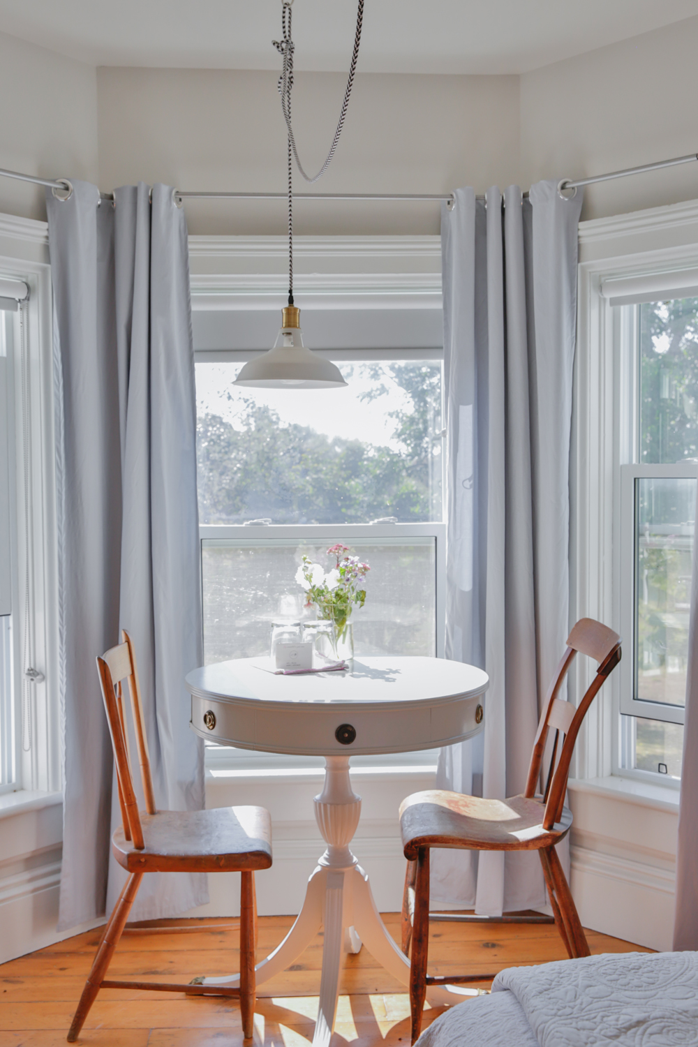 Small vintage white table in bay window with farmhouse chairs