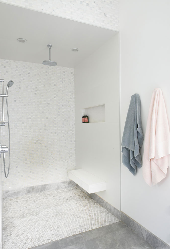 walk-in shower with white floating bench and pink and grey towels